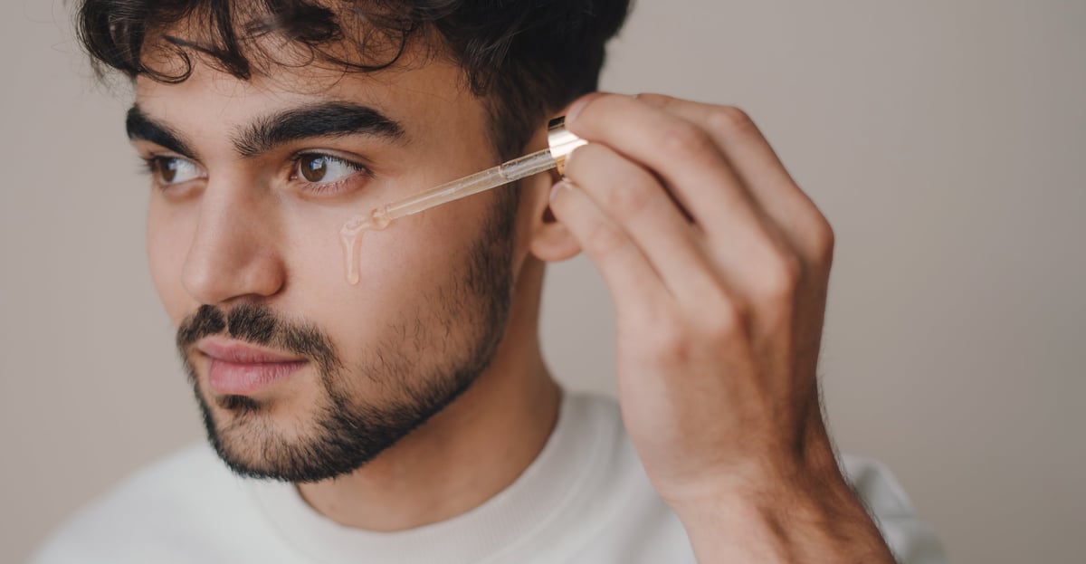Bearded man applying skincare oil to his face during his routine